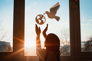 Child hold hands up to a globe with a dove